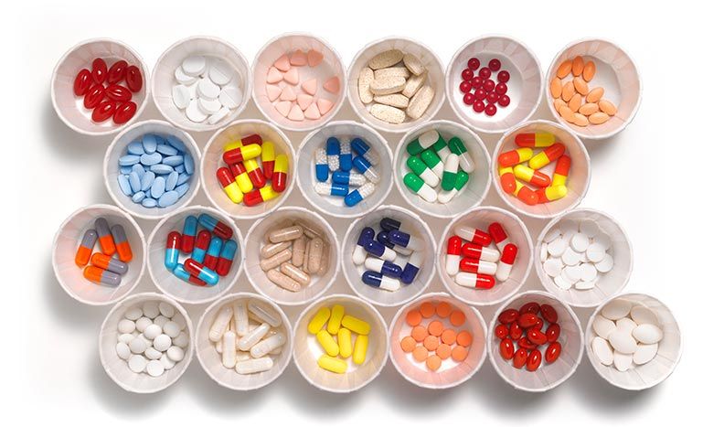 Different colored prescription medication in white medication cups.