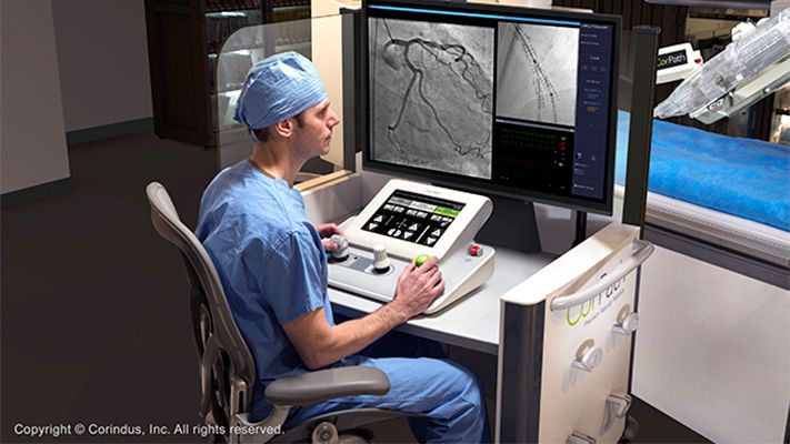 Surgeon sits at desk using a device to navigate the images shown on the screens in front of him.